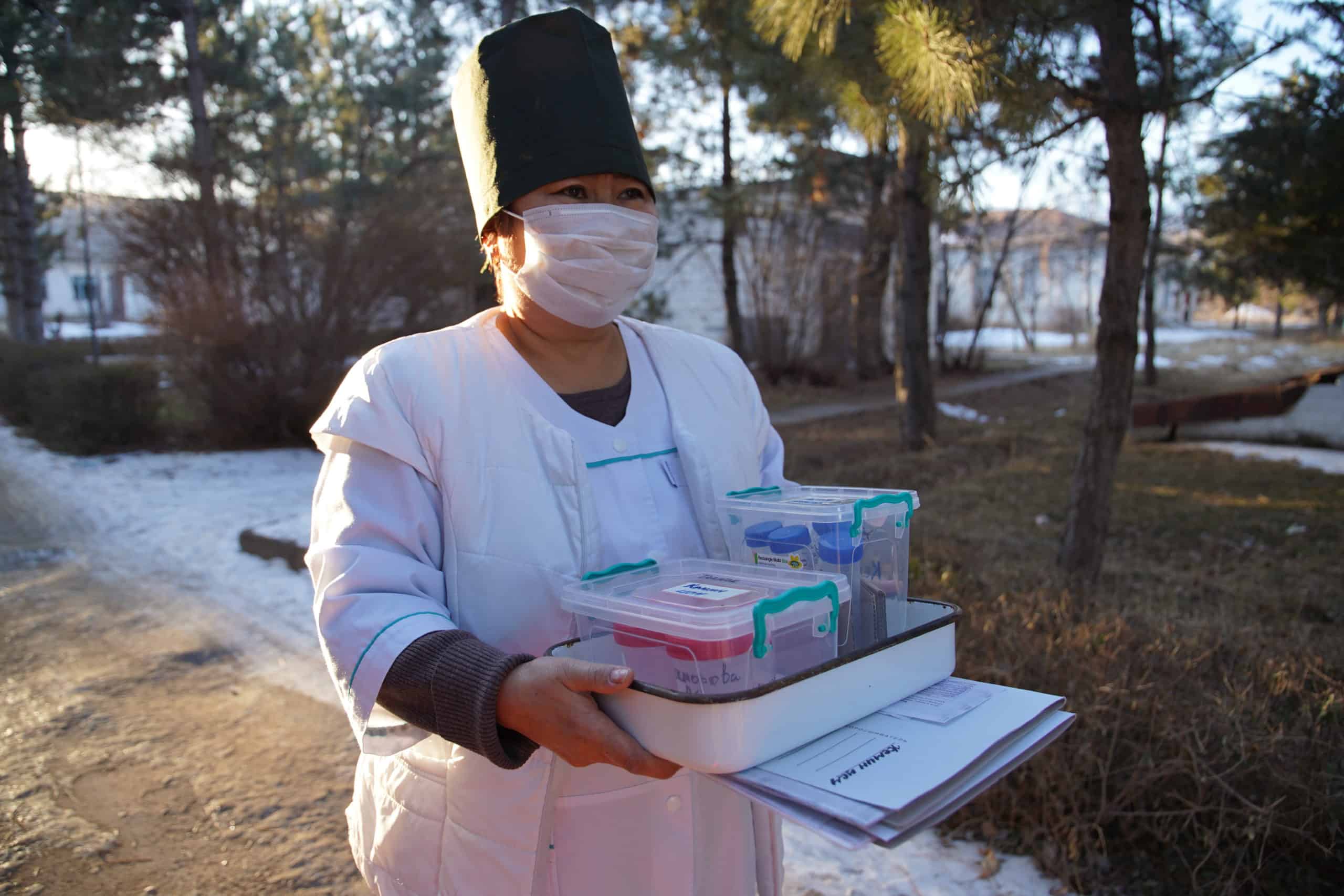 A health worker in Kyrgyz Republic carries supplies while wearing a mask.