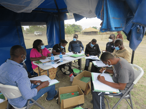 A group of health workers sit under a tent in a rural community in Zambia