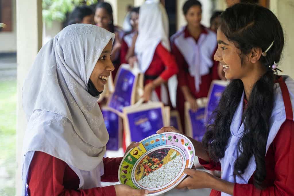 Two young girls in Bangladesh hold a plate to promote nutrition