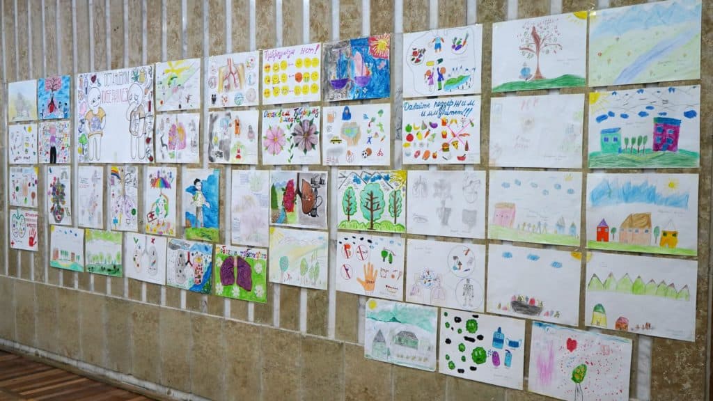 Drawings from the Children's drawing content for World TB Day hang on a wall in display.