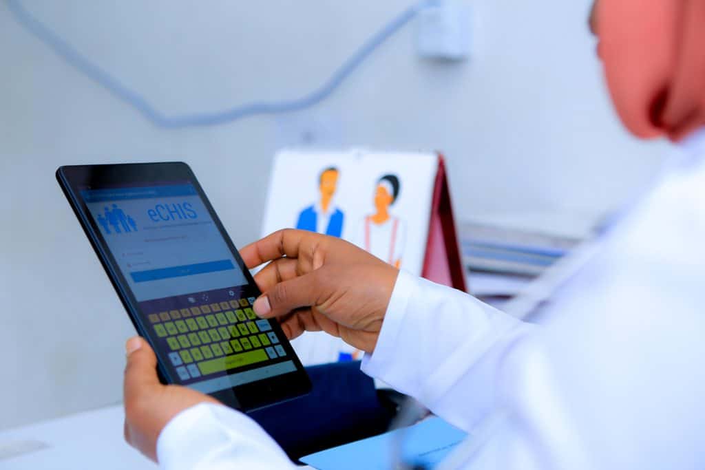 An Ethiopian health worker in a white coat uses a tablet to record medical records.