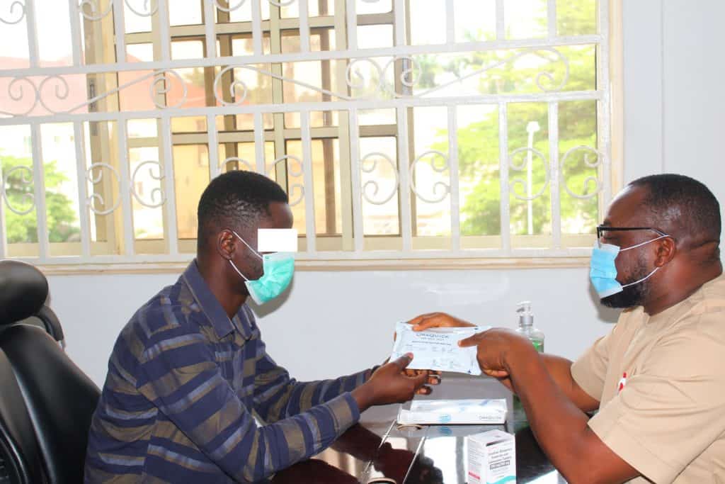 One man passing an HIV self-test kit to another man, both wearing masks.