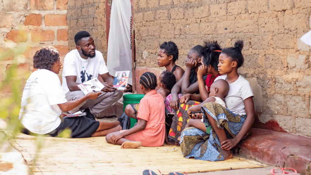 A man sits with children and presents some materials to them in an outdoor setting