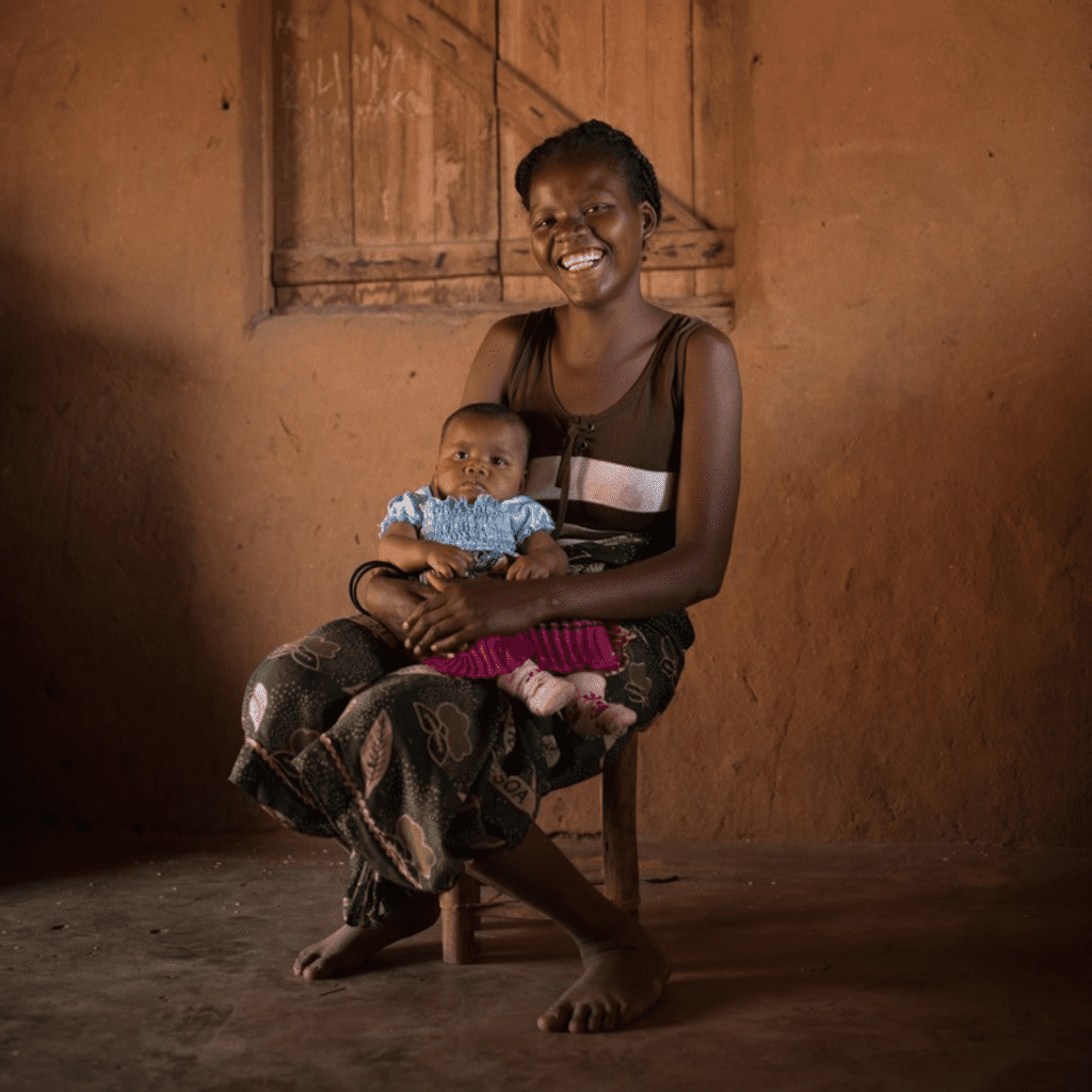 A smiling woman sits in a chair with her baby in her lap.