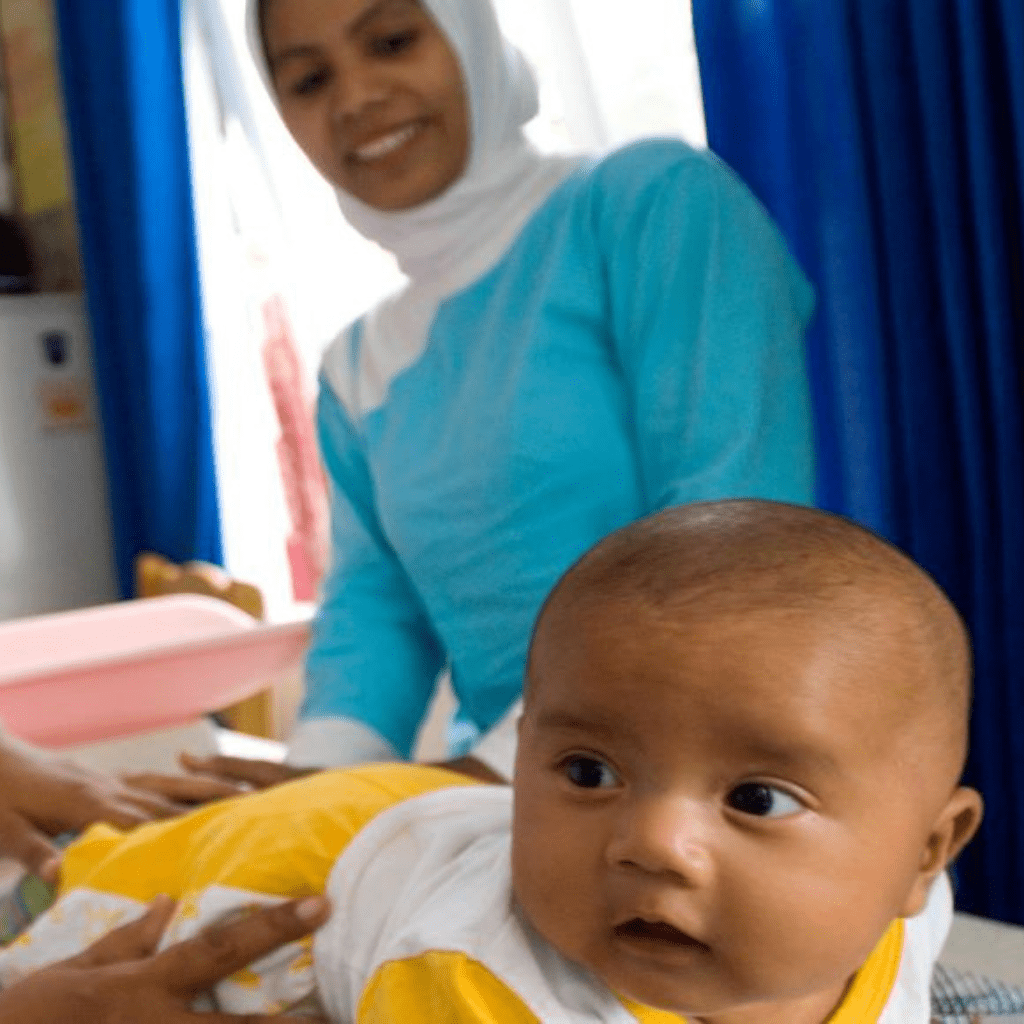 A baby crawls in the foreground with a nurse in the background