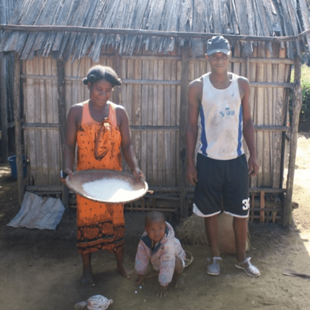 Two parents stand with their baby in a rural village