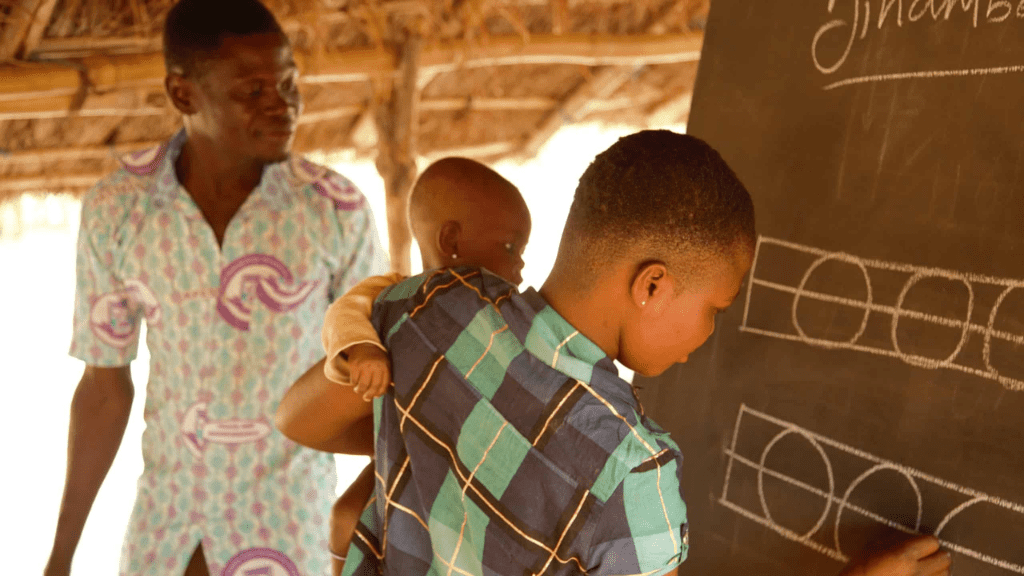 A mother holds her baby while writing on a chalkboard in a Ghana school.