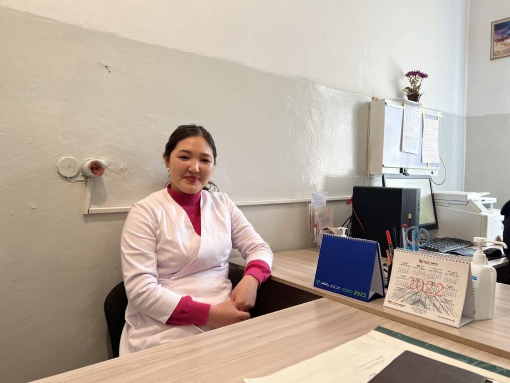 Women in white coat and pink shirt sits behind a desk