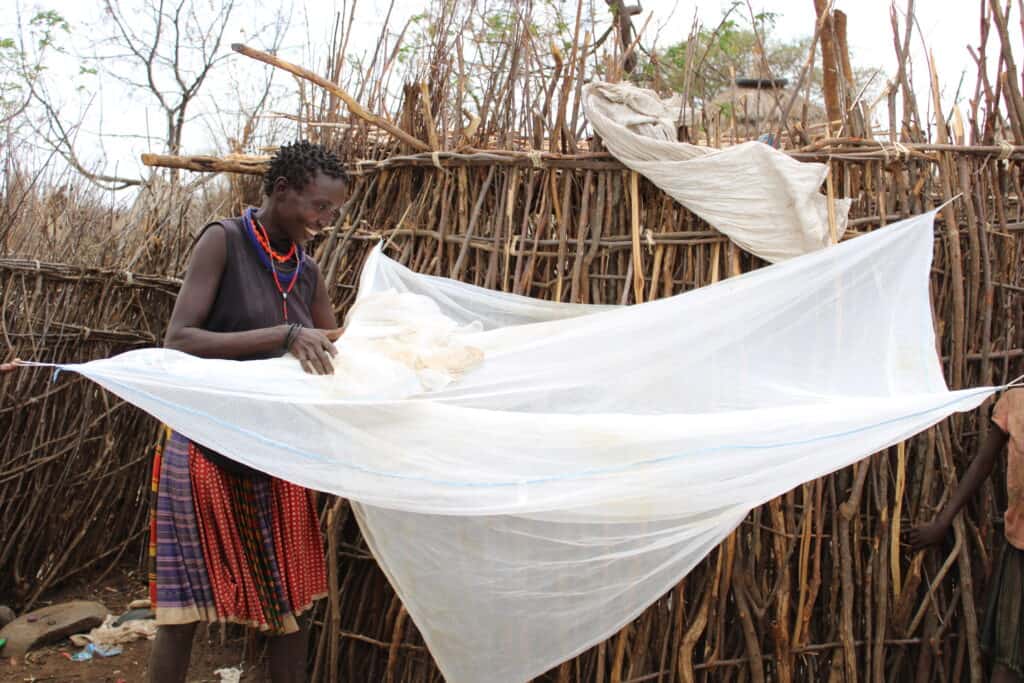 A woman repairs a net outside a hut in Uganda
