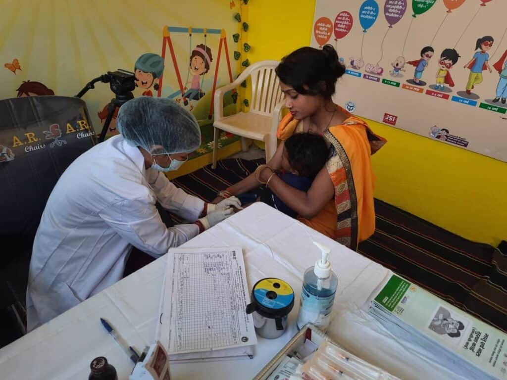 An Indian woman holds a child that is getting vaccinated by medical staff