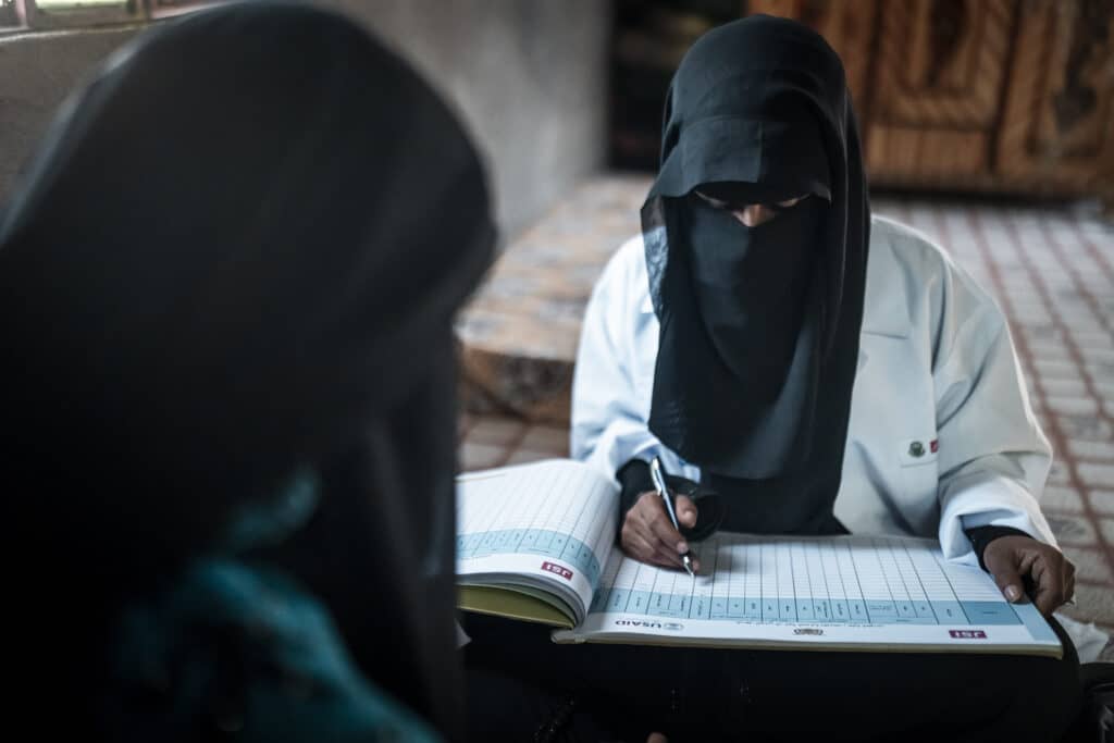 A Yemeni midwife sits before a Yemeni woman, recording her medical data.