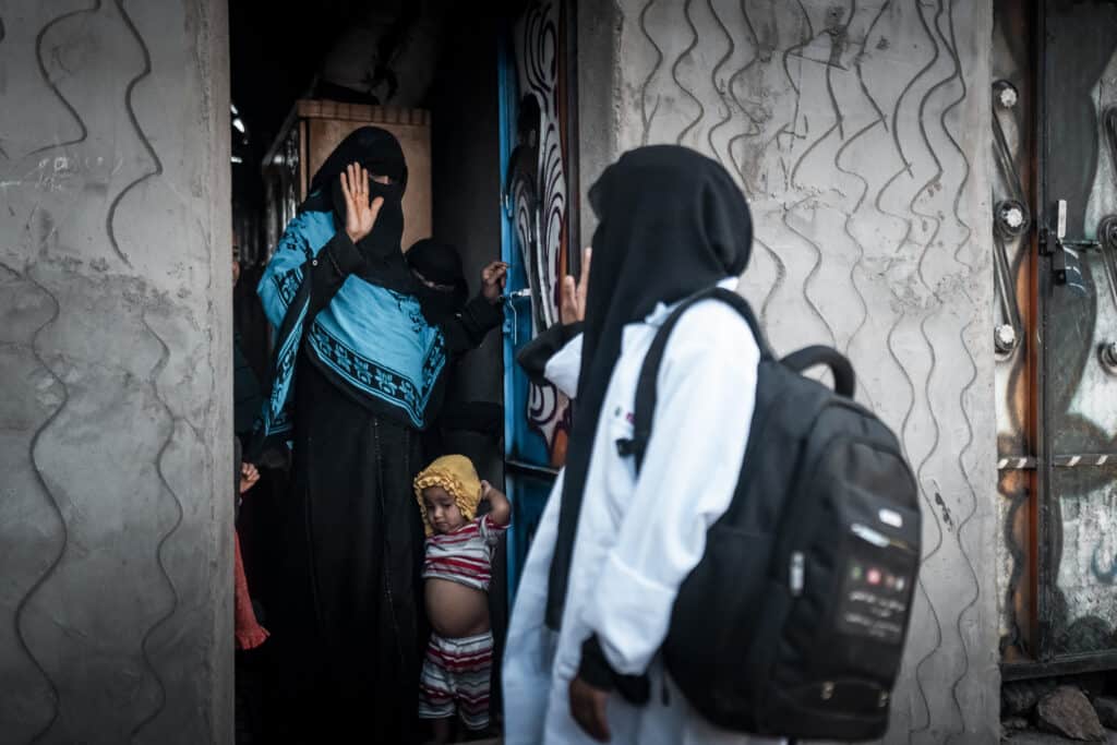 A Yemeni midwife waves goodbye to a mother and child standing in a doorway.