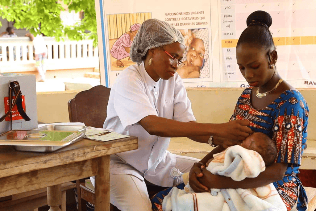 A woman holds a baby while a nurse attends to the baby