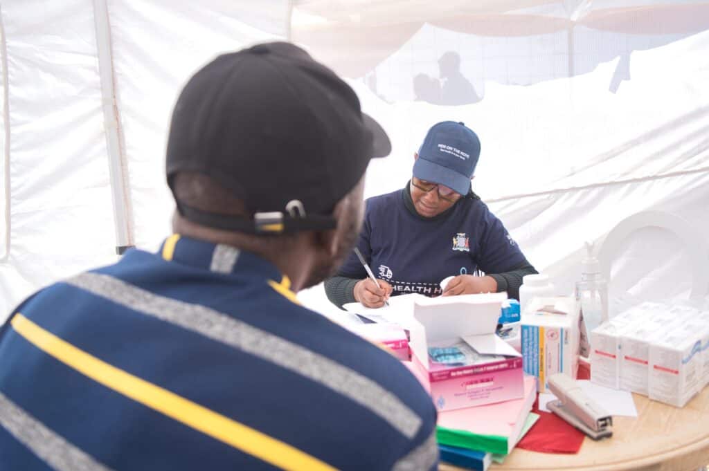 A man sits facing another man filling out paperwork in a tent.