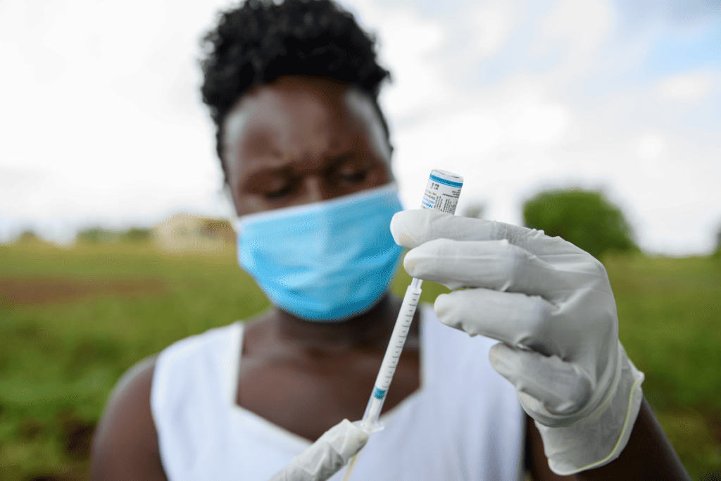 A Ugandan woman wearing a face mask holds an injectible contraceptive up to the camera.