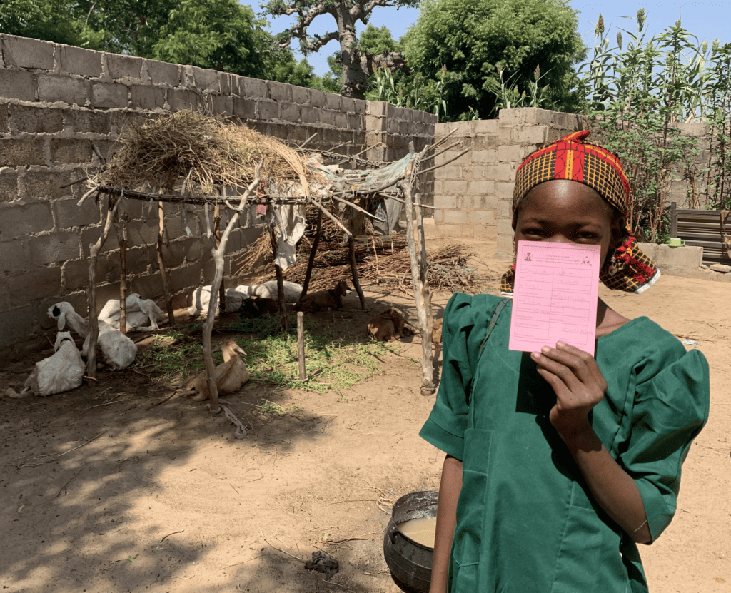 Young Nigerian girl stands holding her vaccination card outside