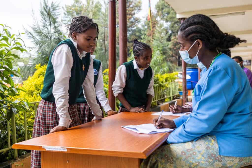 Two girls stand at a table registering for their vaccinations with health care workers