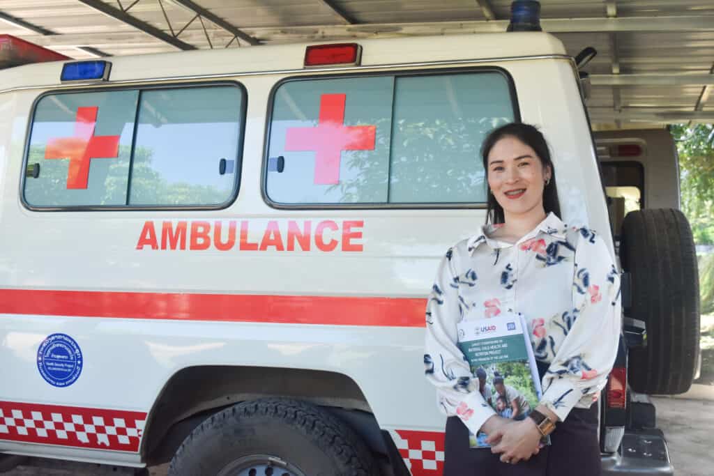 A female health worker stands in front of an ambulance.