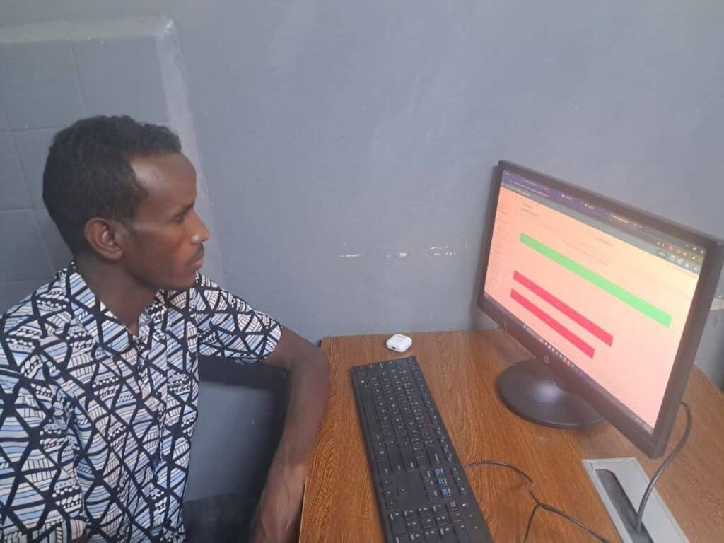 A male health worker looks at a computer screen while sitting at a desk.